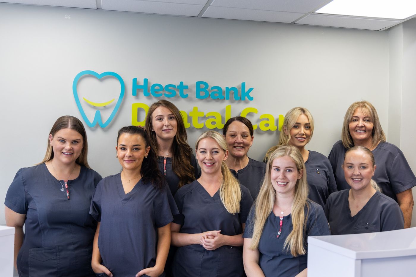 The Hest Bank Dental Care team in front of the practice logo